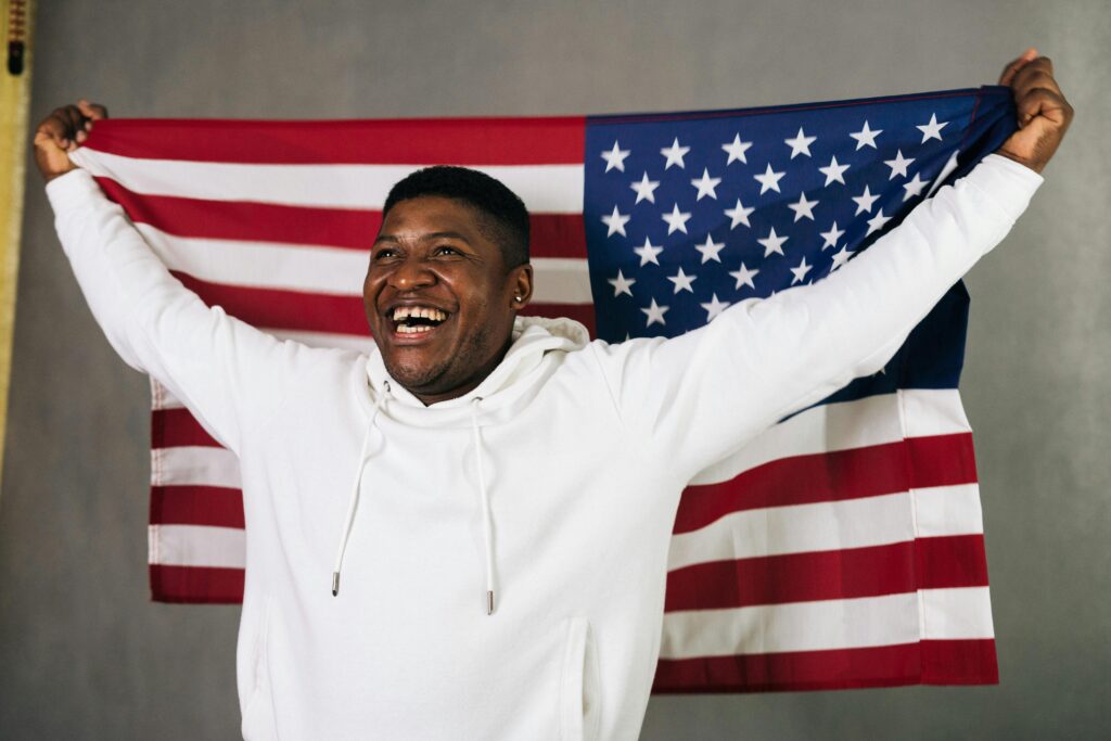 Smiling African American man proudly holds the USA flag, symbolizing patriotism and pride.