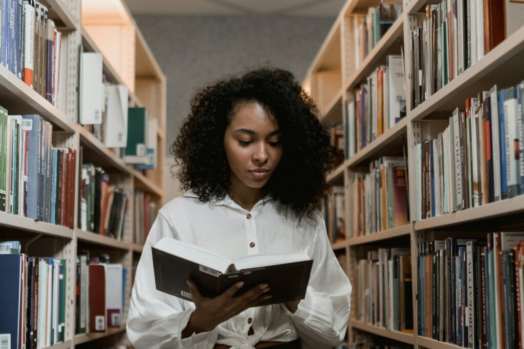 African American woman with curly hair standing in a library reading a book.