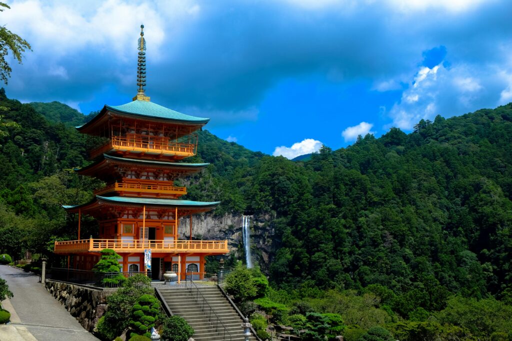 Beautiful view of Kumano Nachi Taisha with a pagoda surrounded by lush green mountains and a waterfall.