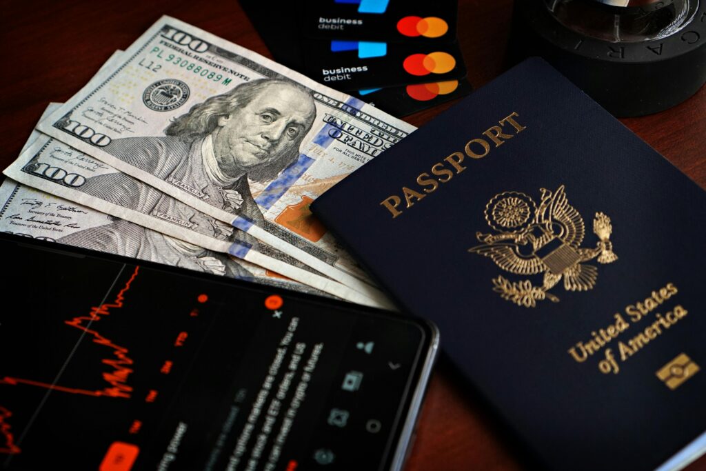 US passport with hundred-dollar bills, credit cards and smartphone showing stock data.