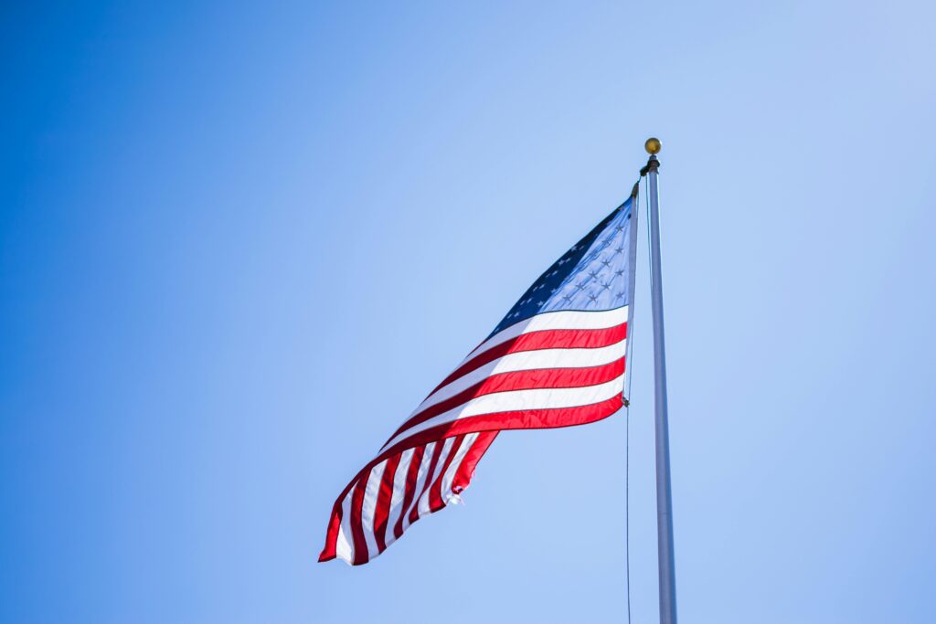 A vibrant American flag waves proudly on a tall flagpole against a clear blue sky.