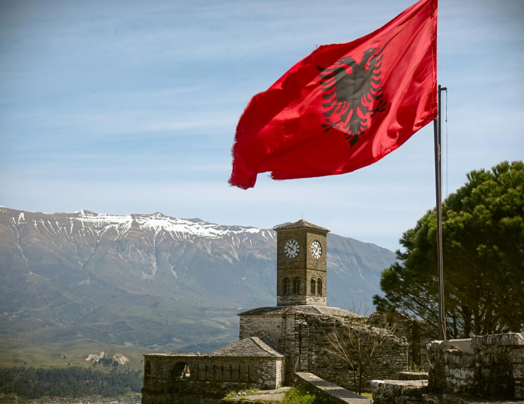 Iconic view of Gjirokaster Fortress featuring the Albanian flag and a clock tower under a blue sky.