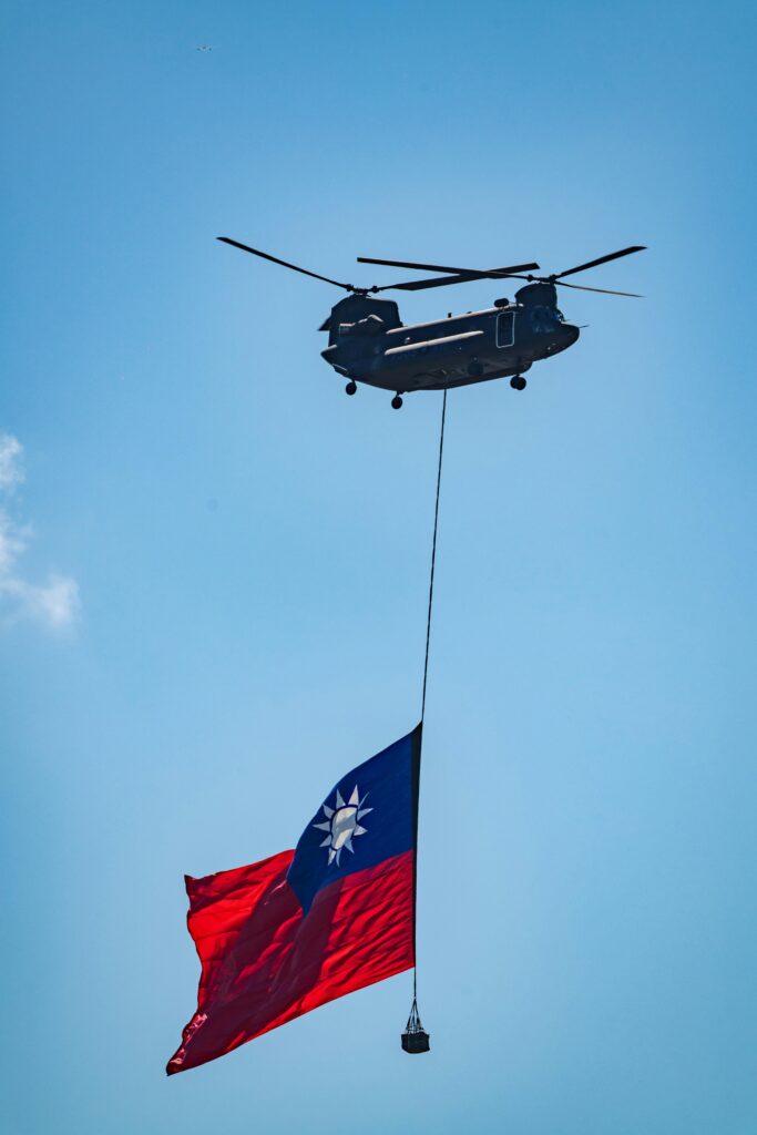 A helicopter hoists the Taiwanese flag against a clear blue sky, symbolizing national pride.