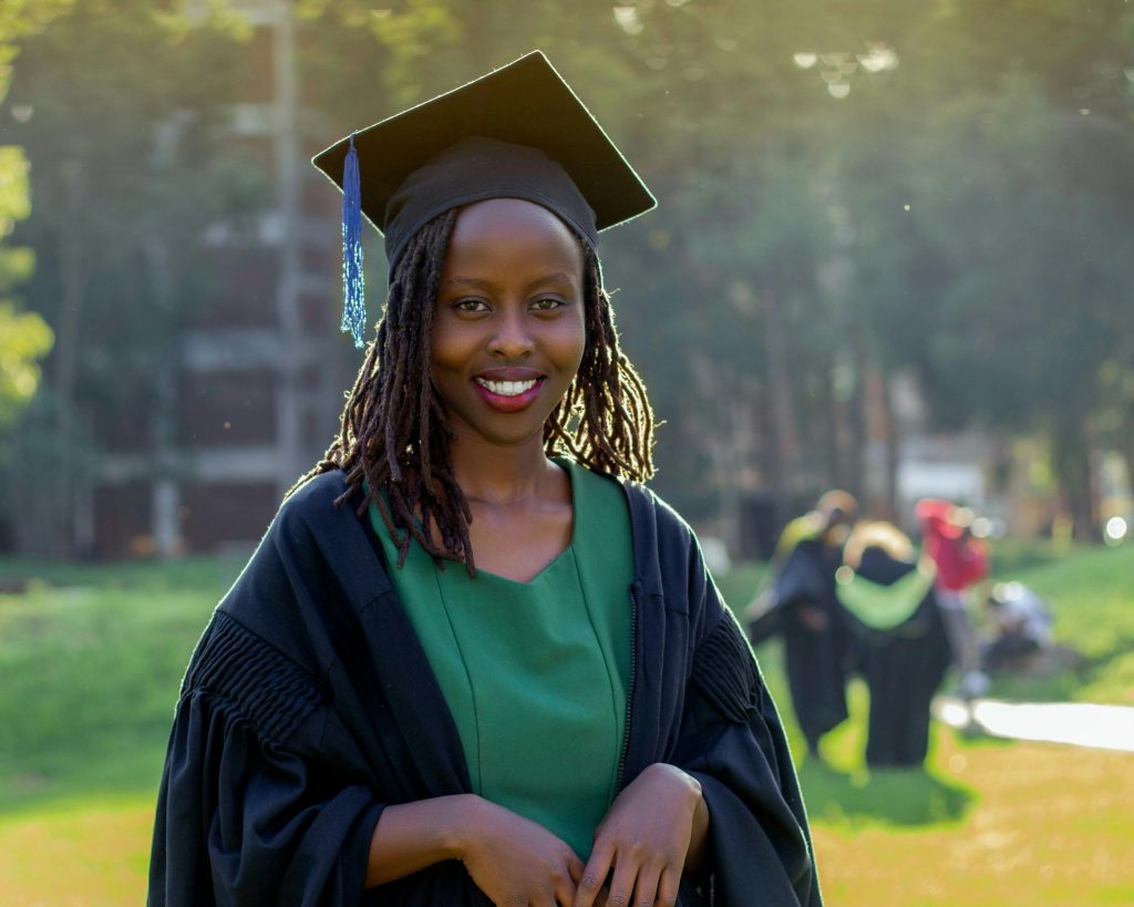 A young woman wearing a graduation cap and gown, smiling outdoors on campus.