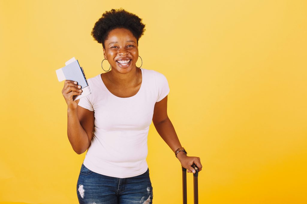 Cheerful woman holding passport ready for travel against a vibrant yellow backdrop.