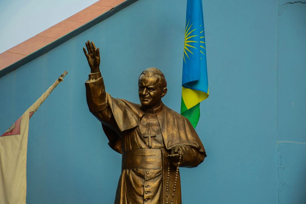A detailed bronze statue of a religious figure stands against a backdrop of blue walls and flags.