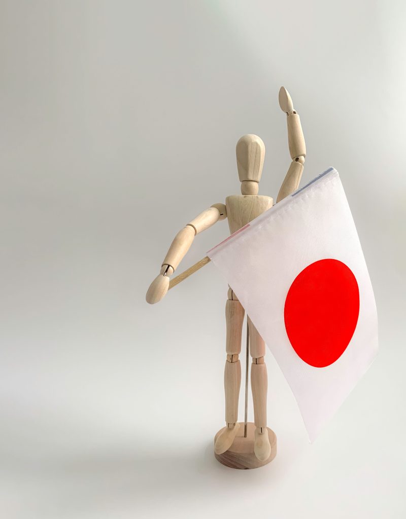 Wooden mannequin figurine holding a Japanese flag against a neutral background.