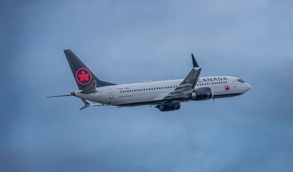 Air Canada airplane soaring through a cloudy sky, showcasing aviation travel.