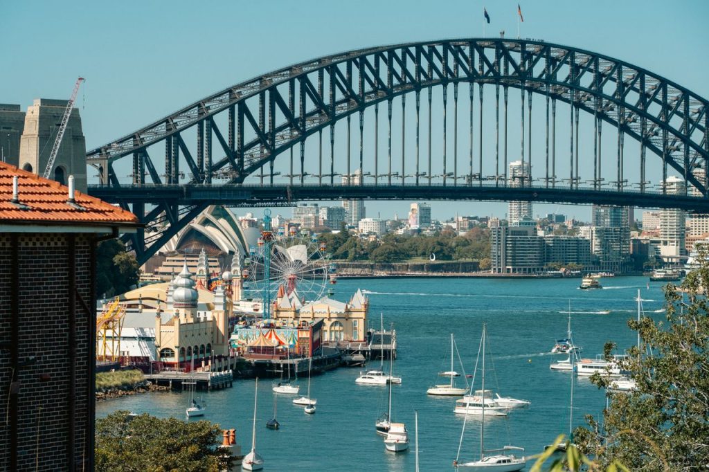 A vibrant view of Sydney Harbour Bridge with Luna Park and sailboats highlighting the iconic skyline.