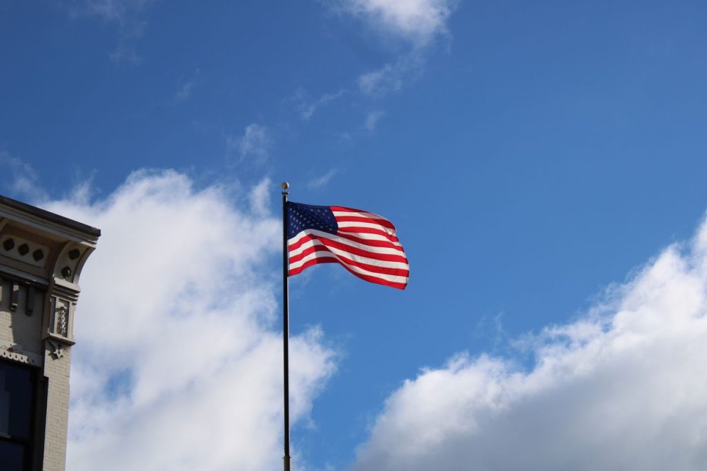 American flag waving on a pole with blue sky and clouds, symbolizing freedom and patriotism.