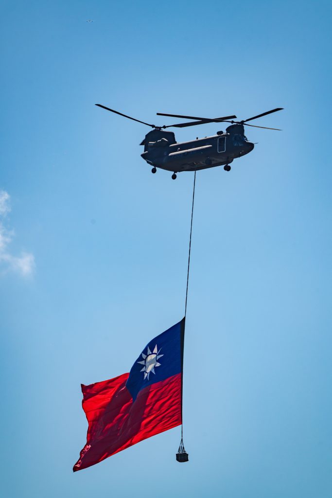 A helicopter hoists the Taiwanese flag against a clear blue sky, symbolizing national pride.