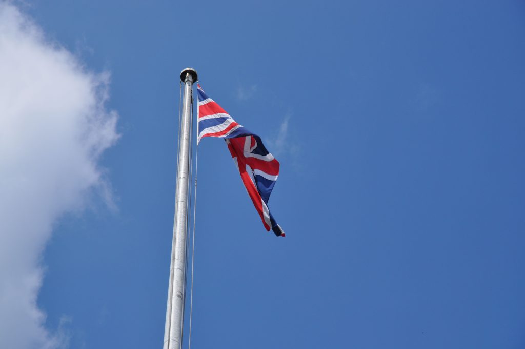 Union Jack flag waving on a flagpole against a clear blue sky in London, UK.