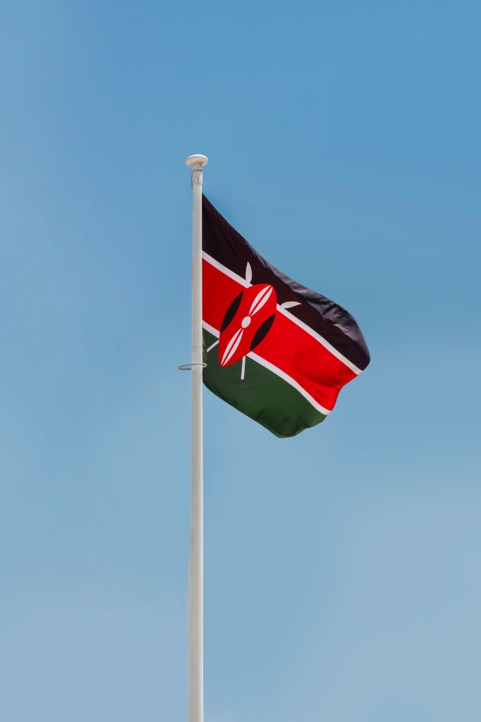 A vertical shot of the Kenyan national flag fluttering against a clear blue sky, symbolizing pride and patriotism.